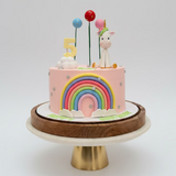 Children's birthday cake with rainbow, unicorn, and number 5 decoration on a wooden stand.